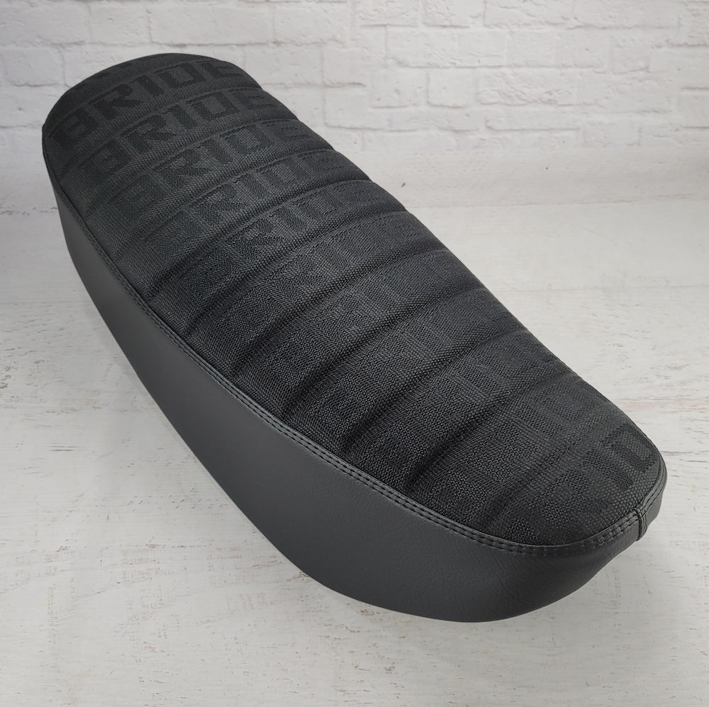 Black BRIDE fabric Honda DAX 125 tuck-and-roll seat cover with tonal stitching and black sides, handmade by Cheeky Seats