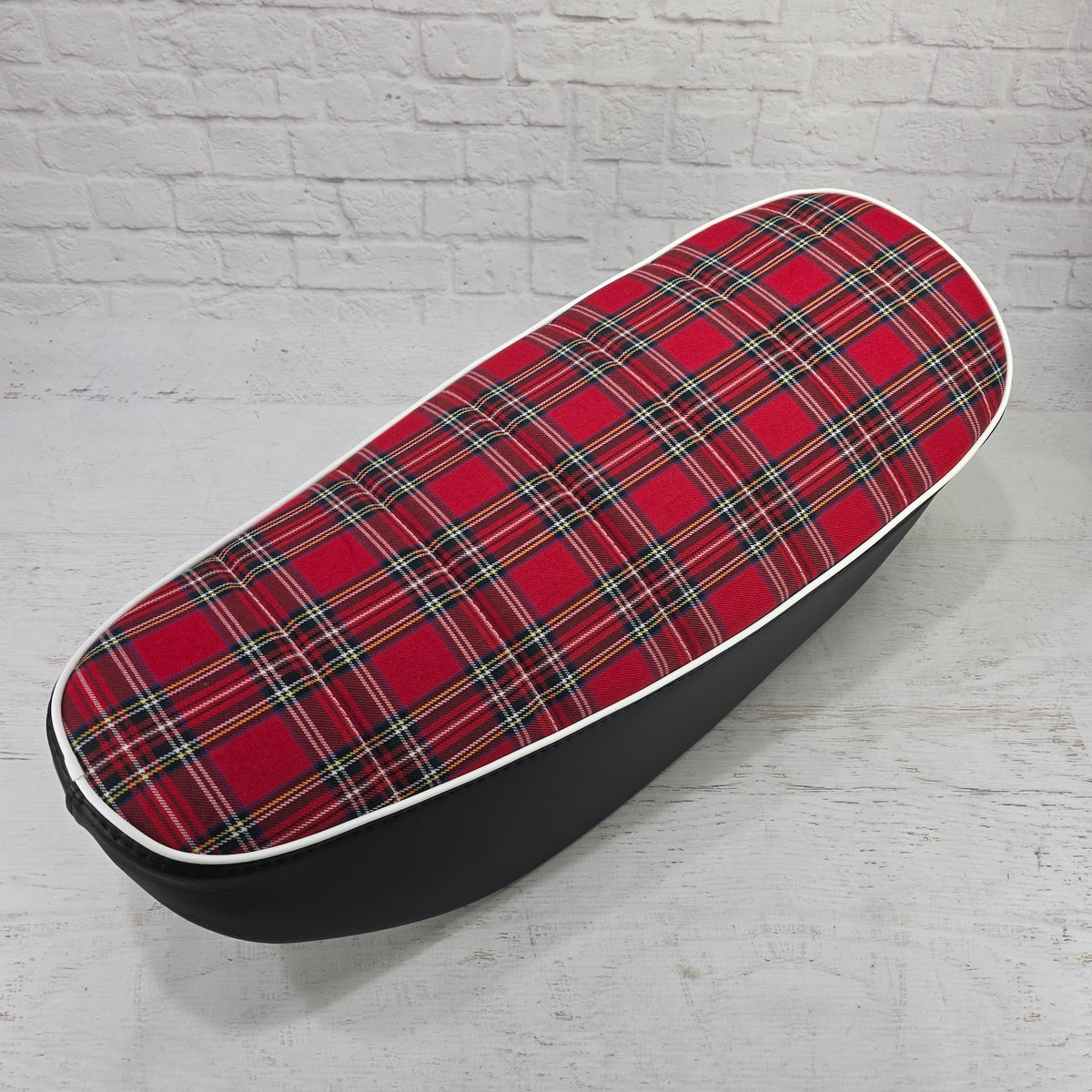 Angled view of a red tartan plaid Honda DAX 125 seat cover with white piping and black side panels, handmade by Cheeky Seats