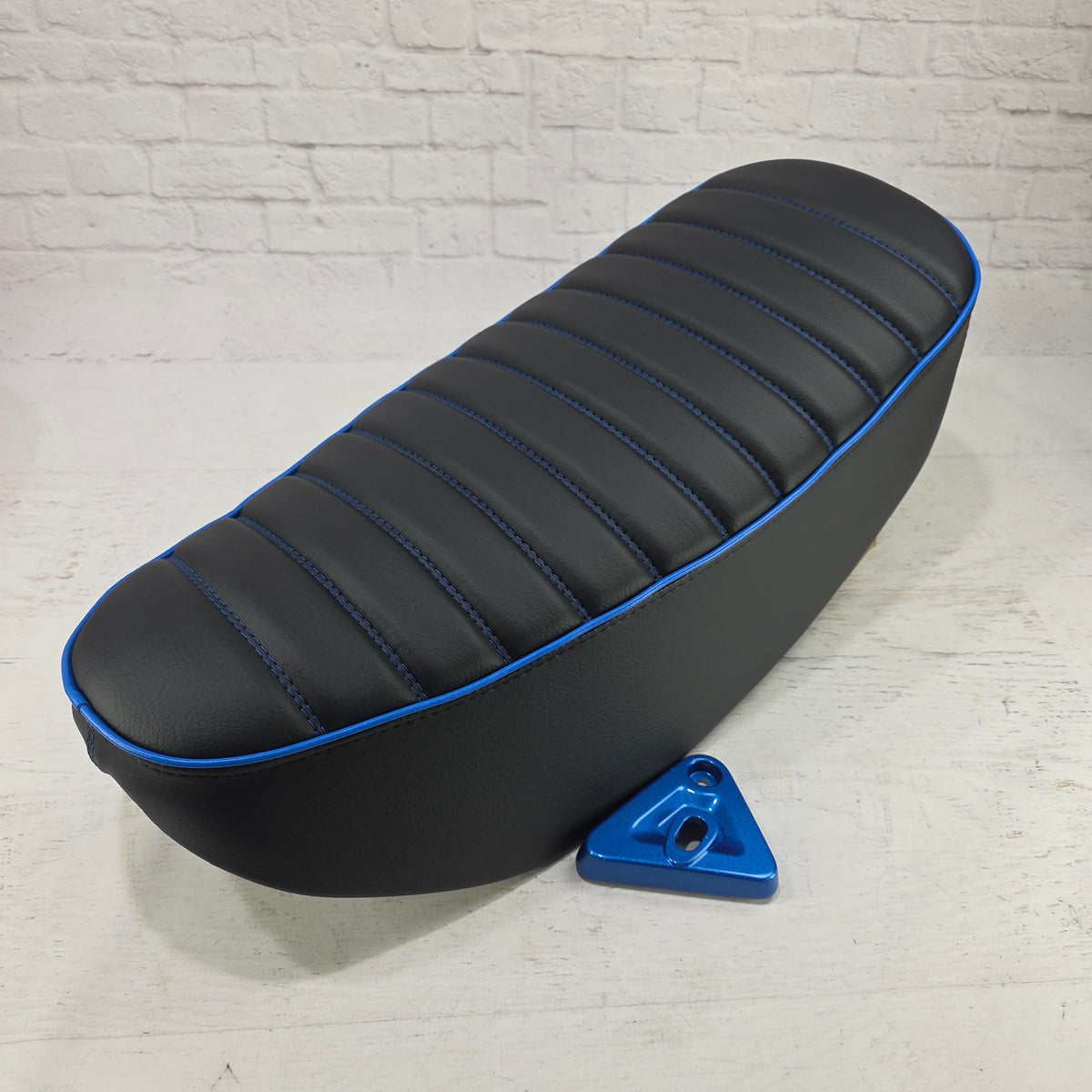 Black double-stitched Honda DAX 125 tuck-and-roll cover with vivid blue piping and matching mounting bracket, handmade by Cheeky Seats