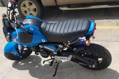 Candy Blue Grom parked on a concrete surface with a vehicle in the background. With Cheeky Seats tuck and roll seat cover