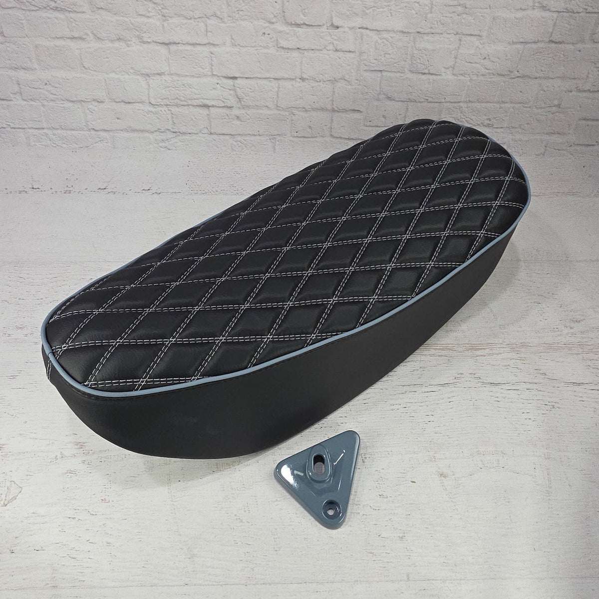 Black double-diamond Honda DAX 125 seat cover with white stitching, pale blue piping and gray lock bracket, handmade by Cheeky Seats