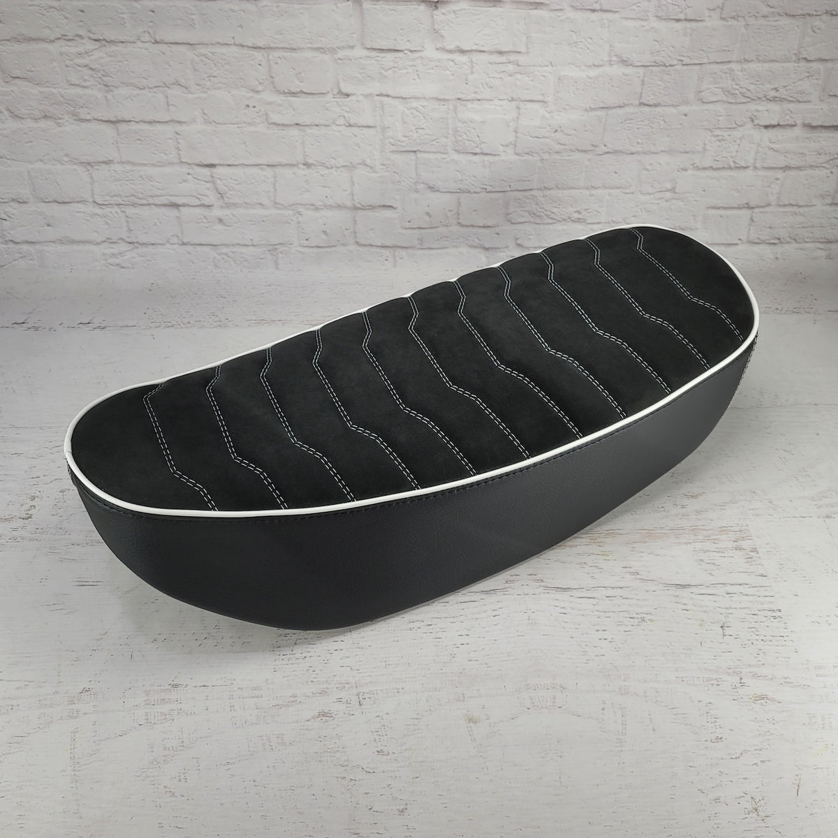 Angled side view of a black Alcantara Rayas Honda DAX 125 cover with white wave stitching and piping, handmade by Cheeky Seats